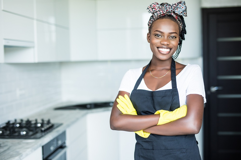 Smiling african american housewife in apron with arms crossed cleaning at home