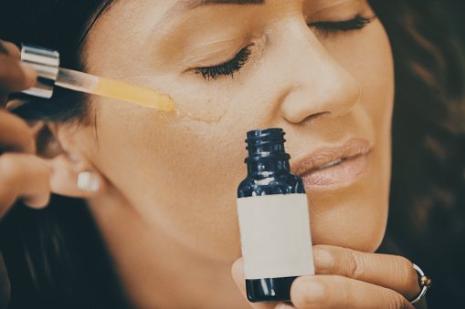Close up of mid adult woman applying face serum on her face.