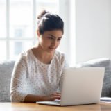 Focused Indian woman using laptop at home, looking at screen