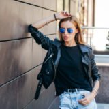 Girl wearing black t-shirt, glasses and leather jacket posing ag
