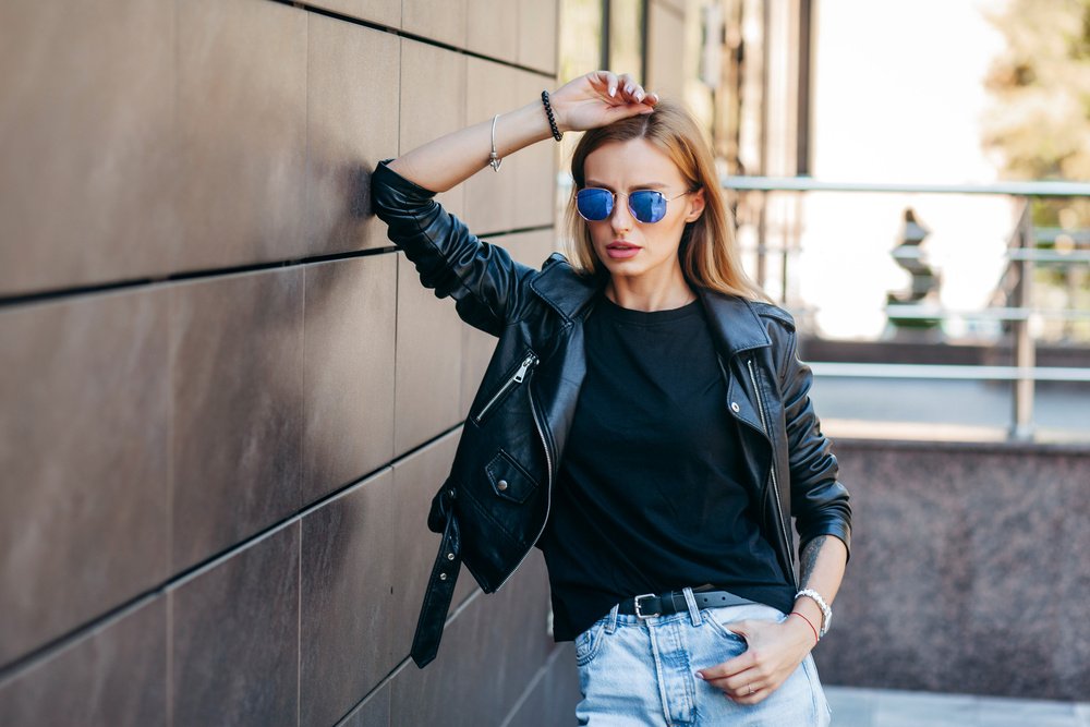 Girl wearing black t-shirt, glasses and leather jacket posing ag